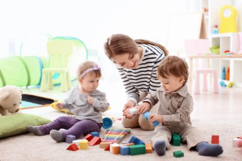 Young nanny playing with little children, indoors 